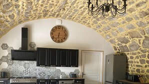 Una cocina con pared de piedra, un reloj de madera y una araña.