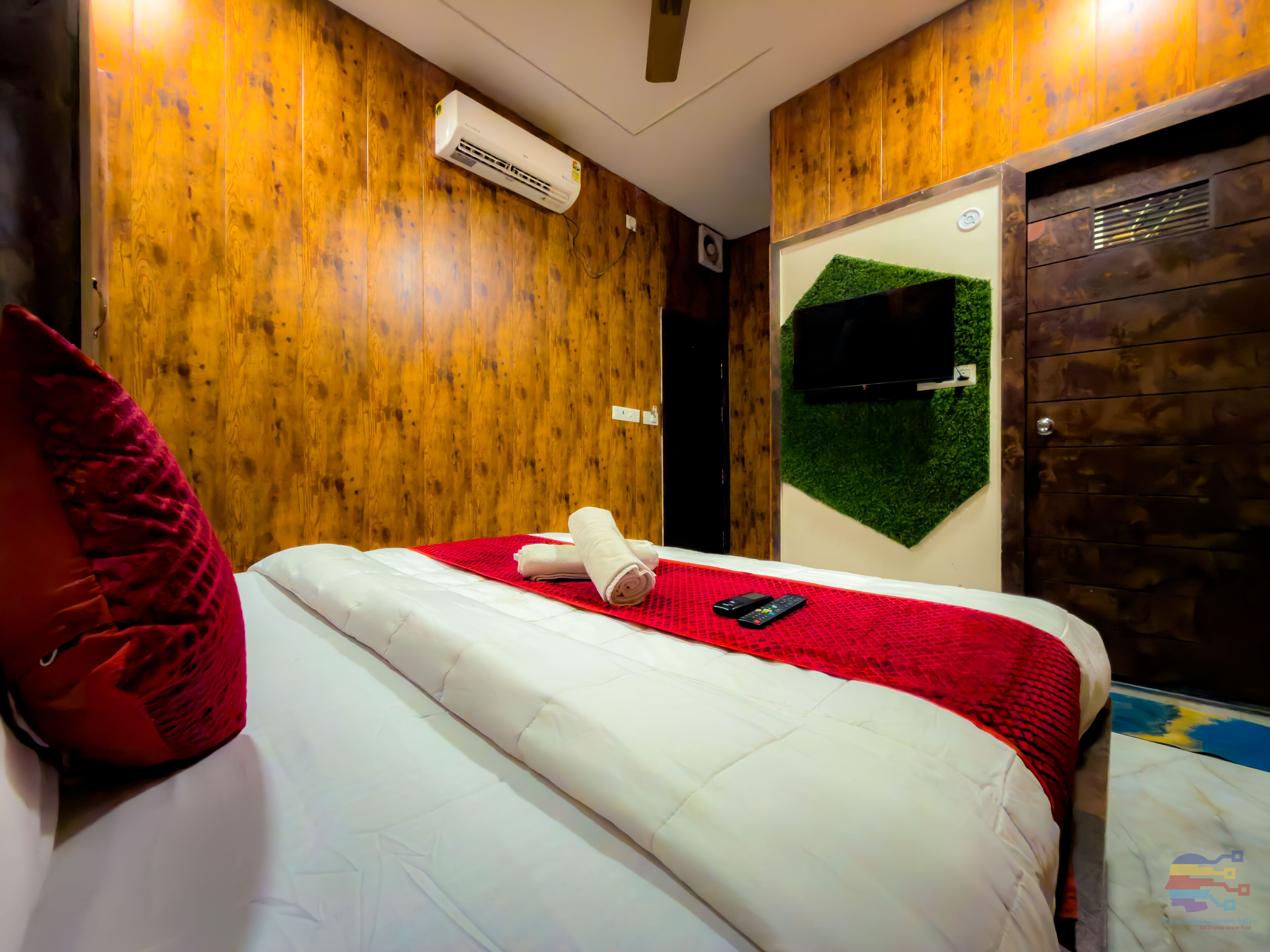 Camera d'albergo con parete in legno, un letto con biancheria bianca, un cuscino rosso, un telecomando e una TV a parete.