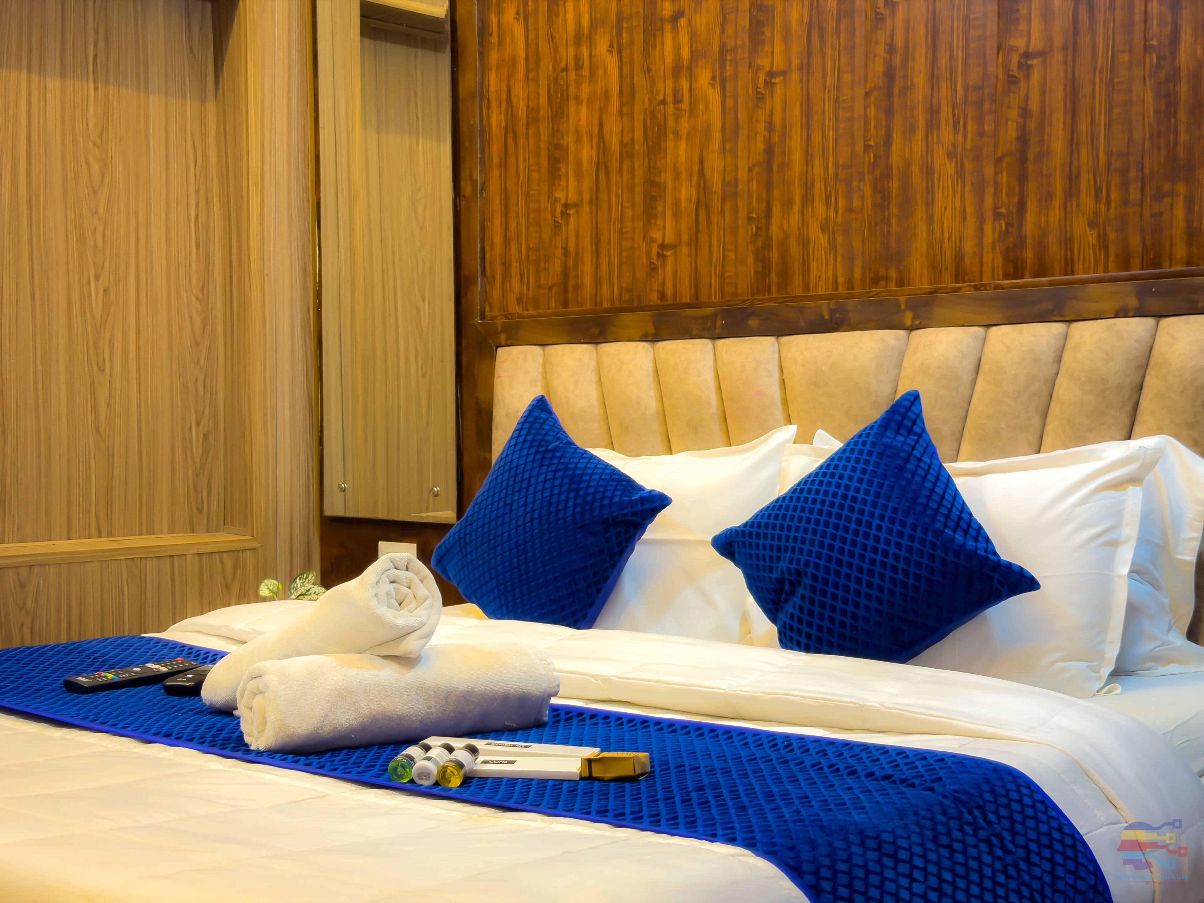 A hotel room with a bed, pillows, a blanket, a remote control, and a bottle.