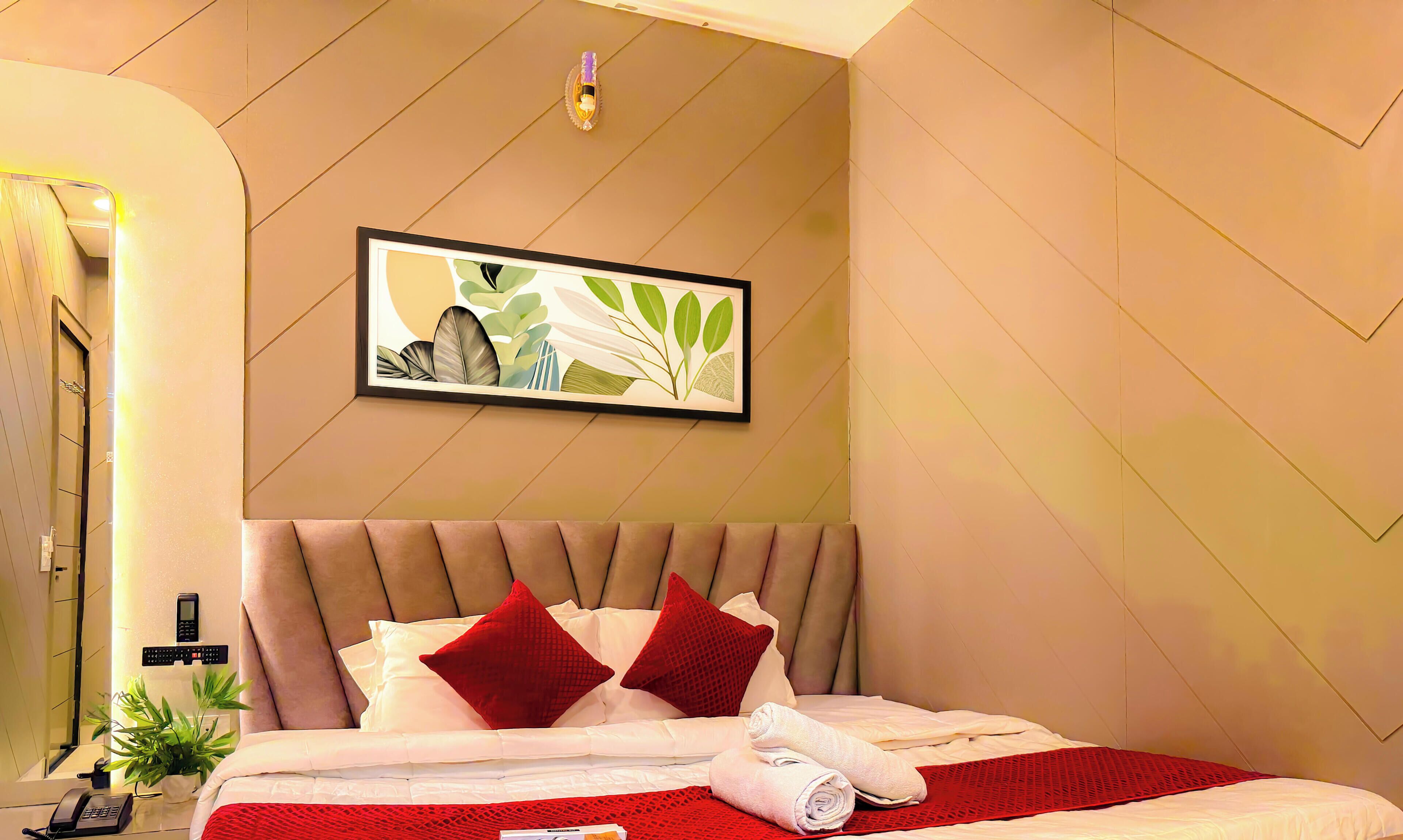 A hotel room with a bed, a wall-mounted artwork, a telephone, and a small plant.