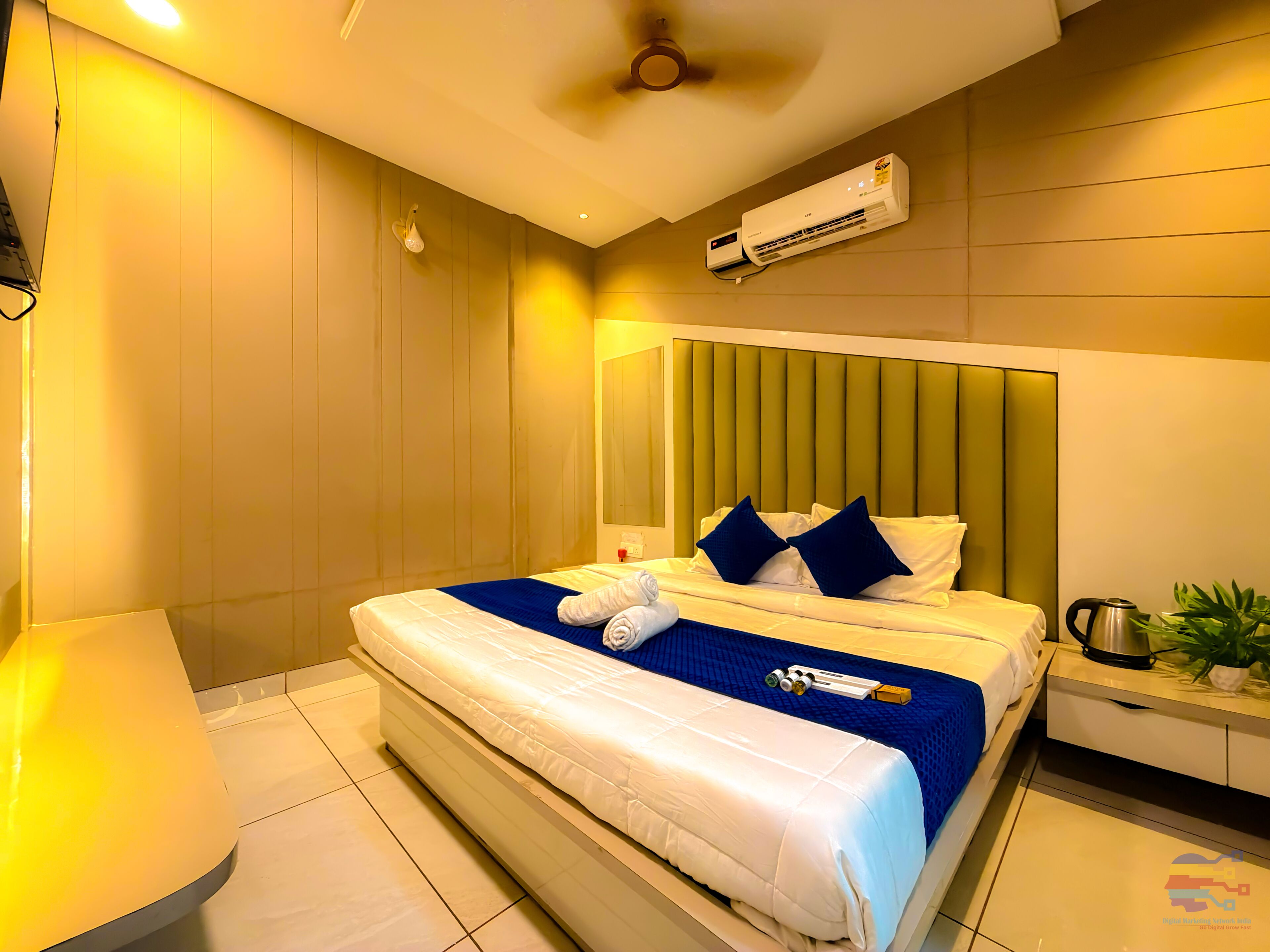 Quarto de hotel com cama, mesa de cabeceira, aparelho de ar condicionado e ventilador de teto.