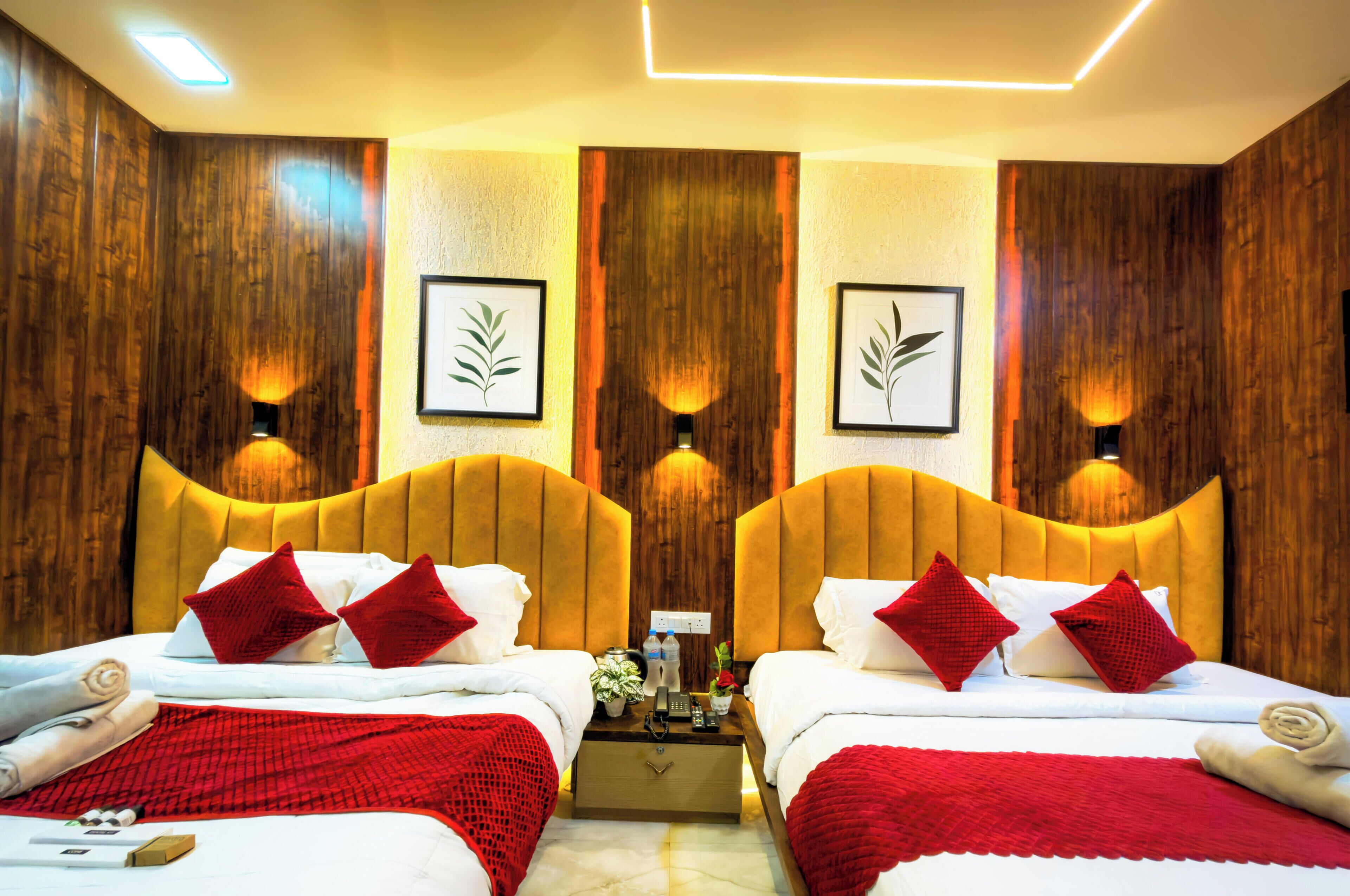 A hotel room with two beds, wooden paneling, red and white bedding, and wall-mounted lights.