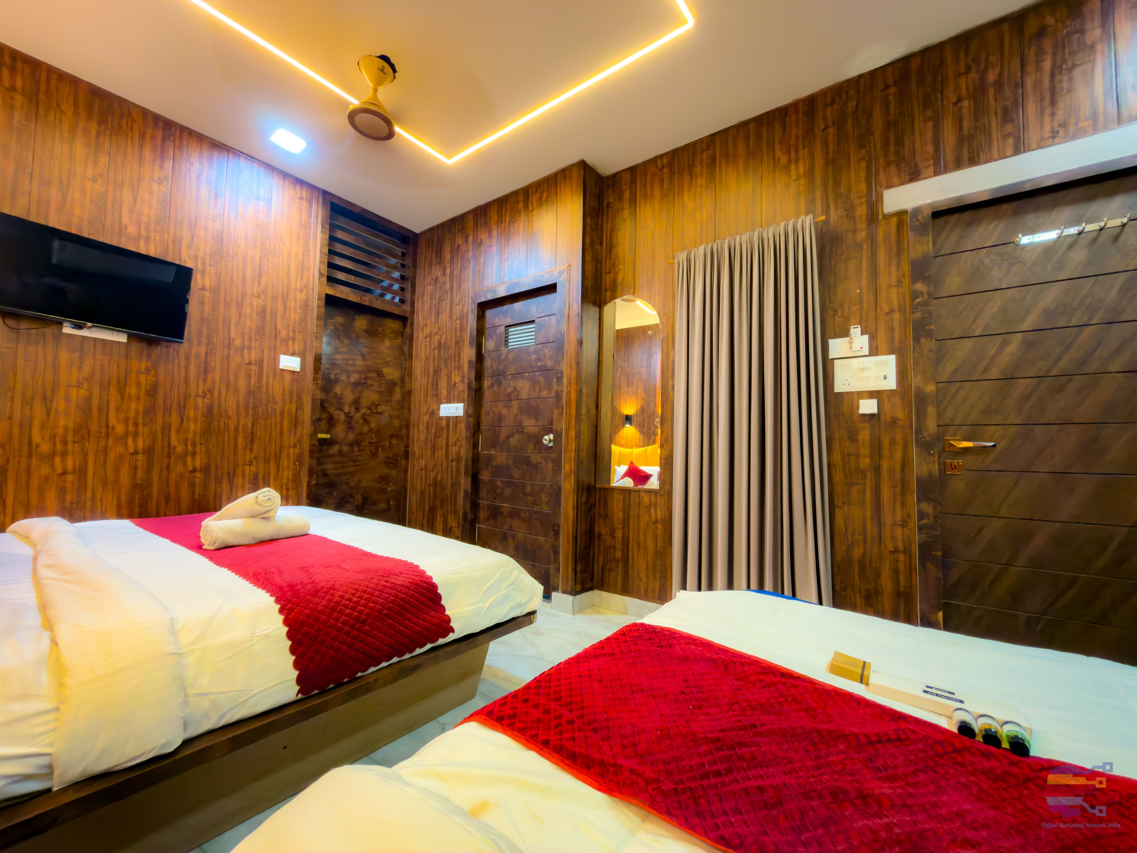 A hotel room with two beds, wooden paneling, a ceiling fan, a TV, and a mirror.