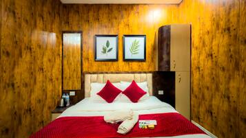 Habitación de hotel con paredes de madera, cama con ropa de cama roja y blanca, dos adornos con hojas enmarcados, una minibar y un armario.