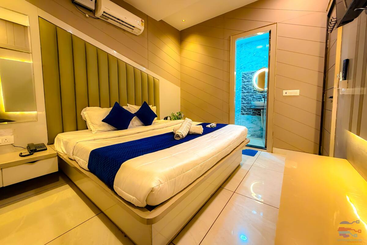 A modern hotel room with a large bed, bedside table, and an air conditioning unit.
