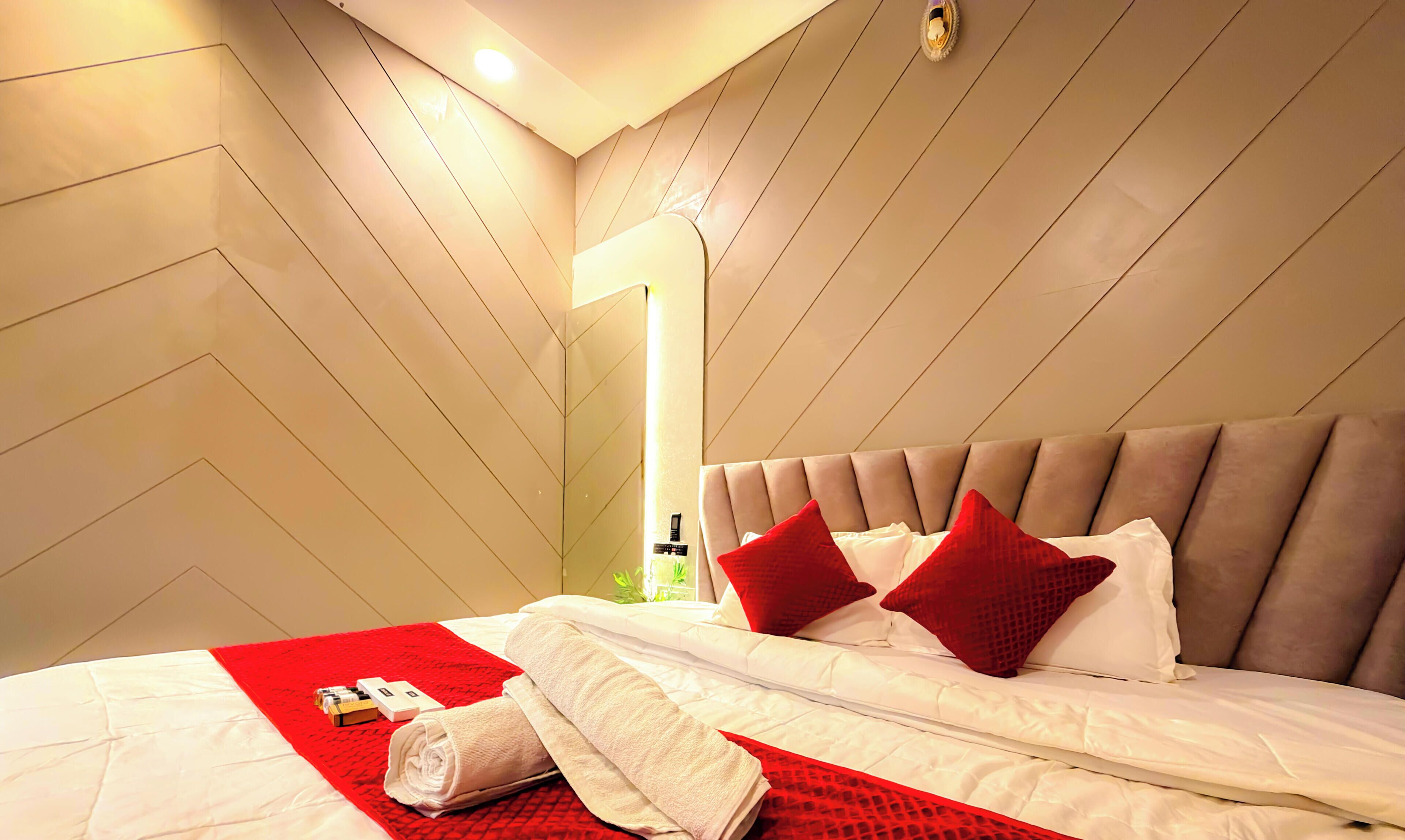 Una habitación de hotel con cama, ropa de cama roja y blanca, una manta roja y una mesita de noche con artículos de aseo.