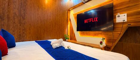 A hotel room with a large bed, a flat-screen TV, wooden paneling, and an air conditioning unit.