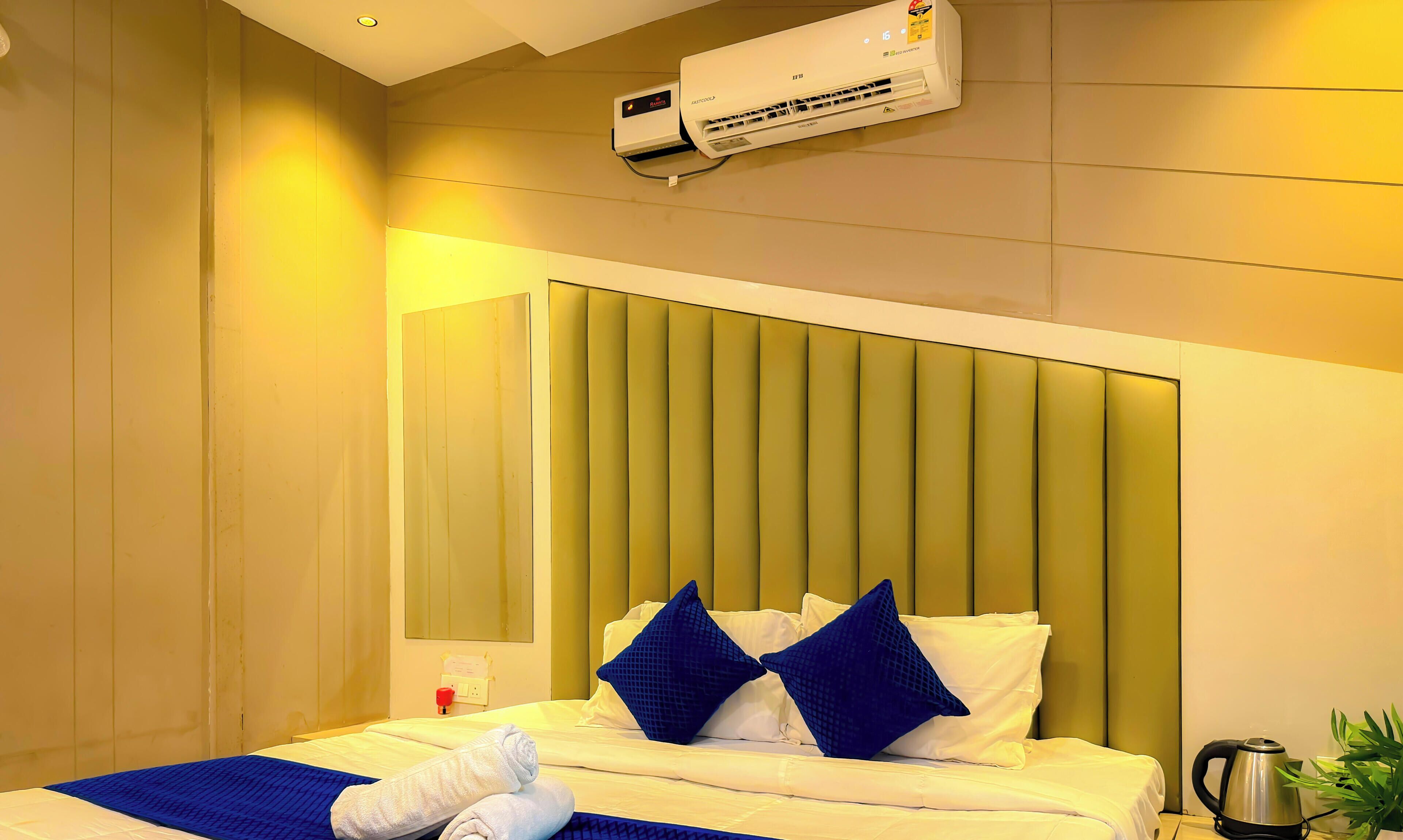 Et hotelværelse med en seng, puder, et natbord med elkedel og en aircondition.