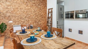A dining area with a wooden table set for four, surrounded by chairs. A stone wall and a white wall with a built-in oven and microwave are visible. - Brat Salions by Interhome (Tossa de Mar)