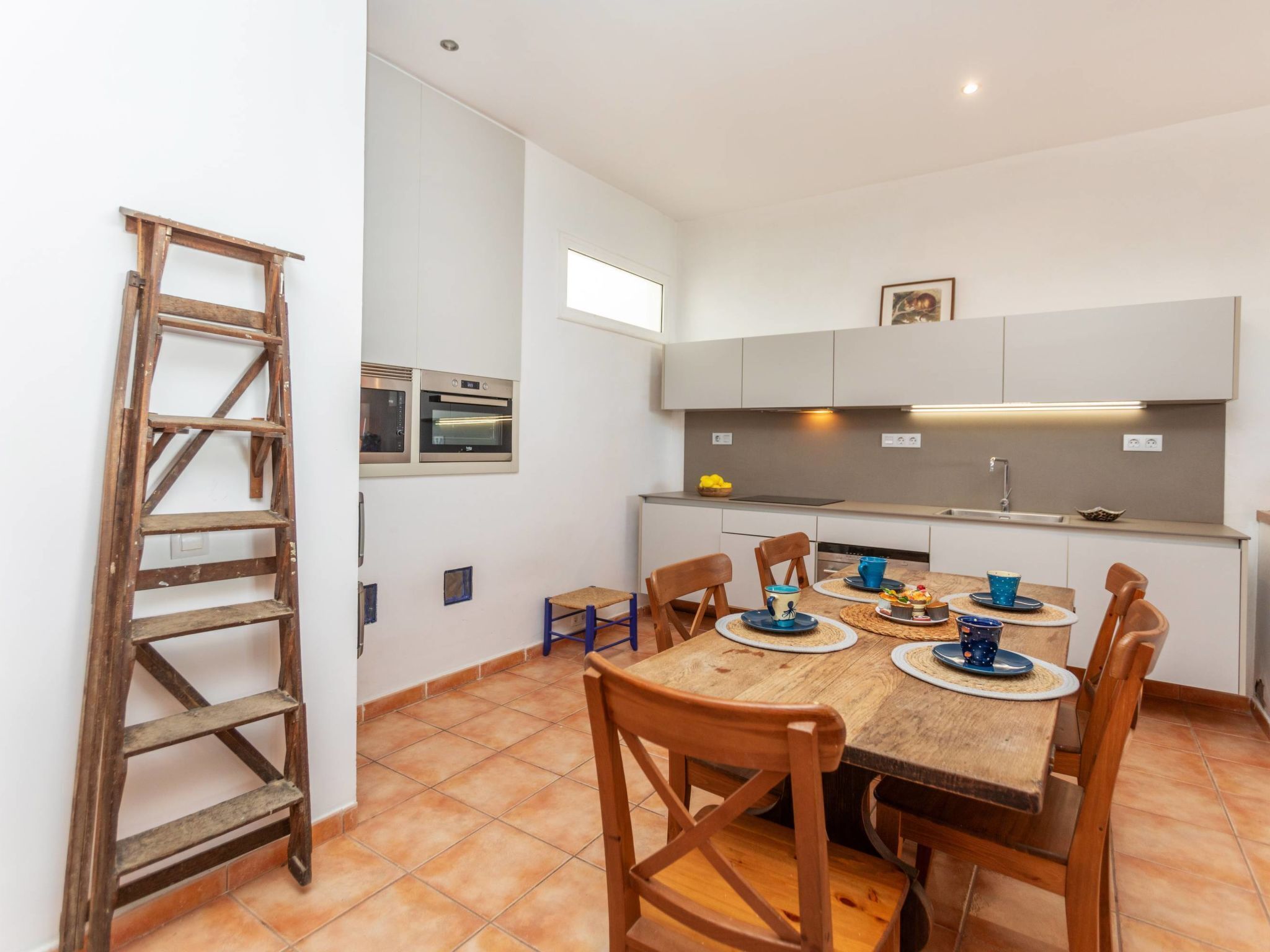 A compact kitchen with white cabinets, a built-in oven, and a dining area with a wooden table and chairs.