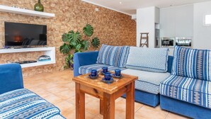 A living room with a stone wall, a blue sofa, a wooden coffee table, and a television on a white shelf. - Brat Salions by Interhome (Tossa de Mar)
