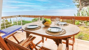 A wooden table set for two with a bowl of fruit, glasses, and plates on a balcony overlooking a body of water. - Brat Salions by Interhome (Tossa de Mar)