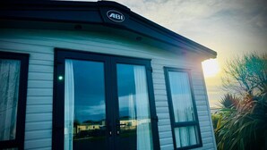 A mobile home with a large window and a door, a sign with the letters "ABI" on the roof, and a sunset in the background. - Luxury holiday Home close to Padstow and beautiful beaches  (Saint Merryn)