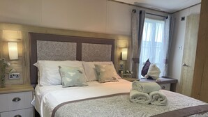 A neatly made bed with patterned bedding and pillows, a bedside table with a lamp, and a window with curtains. - Luxury holiday Home close to Padstow and beautiful beaches  (Saint Merryn)