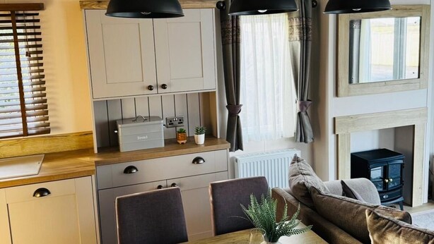 A modern kitchen with white cabinets, a wooden countertop, and a dining area with a wooden table and chairs. There is a black stove in the background. - Luxury holiday Home close to Padstow and beautiful beaches  (Saint Merryn)