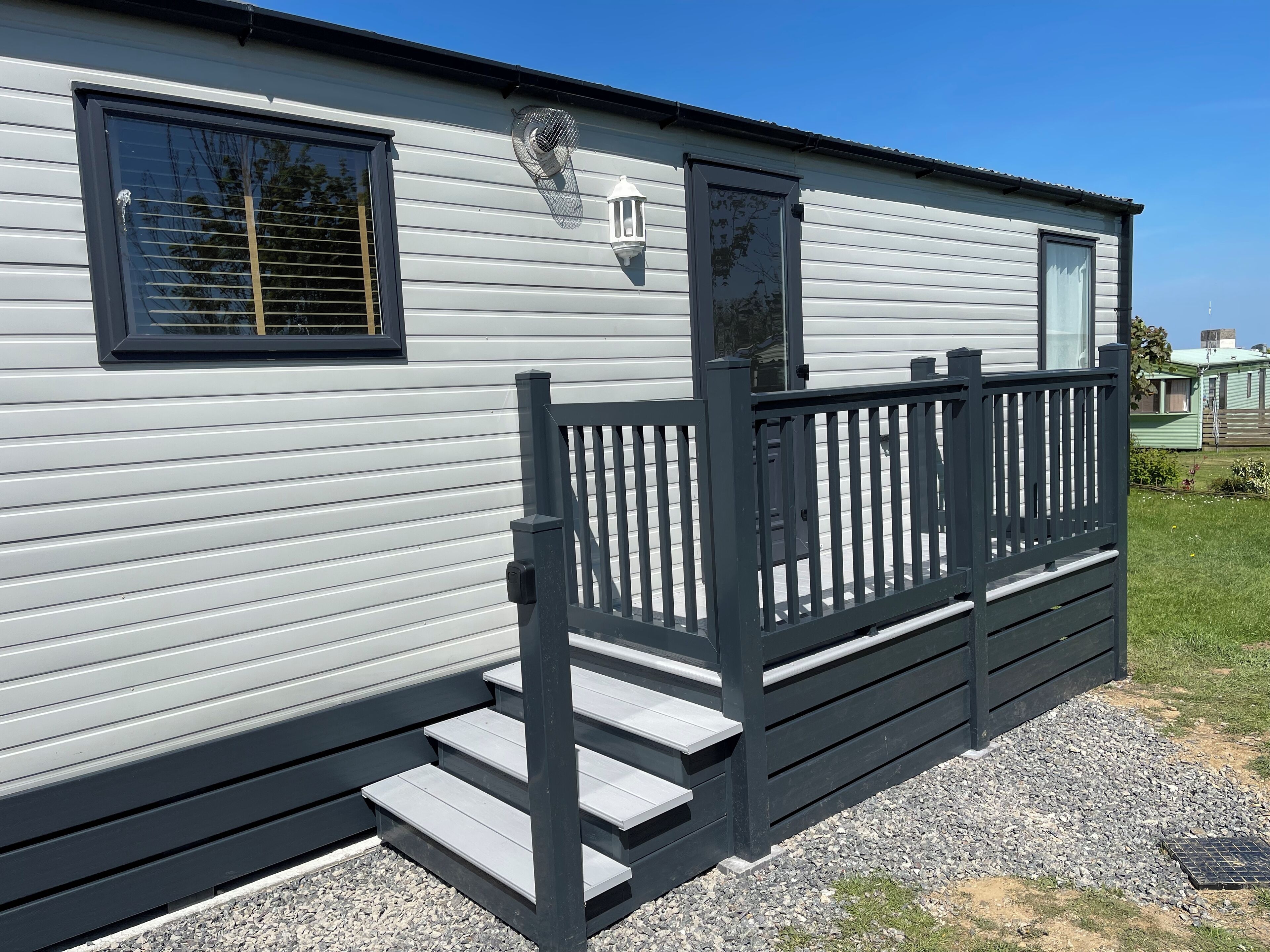 Une maison mobile dotée d’une terrasse à l’avant, d’une fenêtre avec des stores et d’une porte.