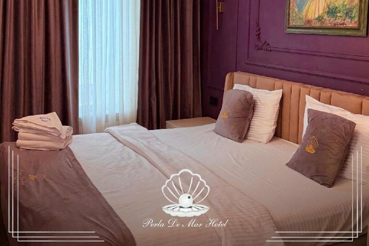 A hotel room with a bed, pillows, a painting, and curtains.
