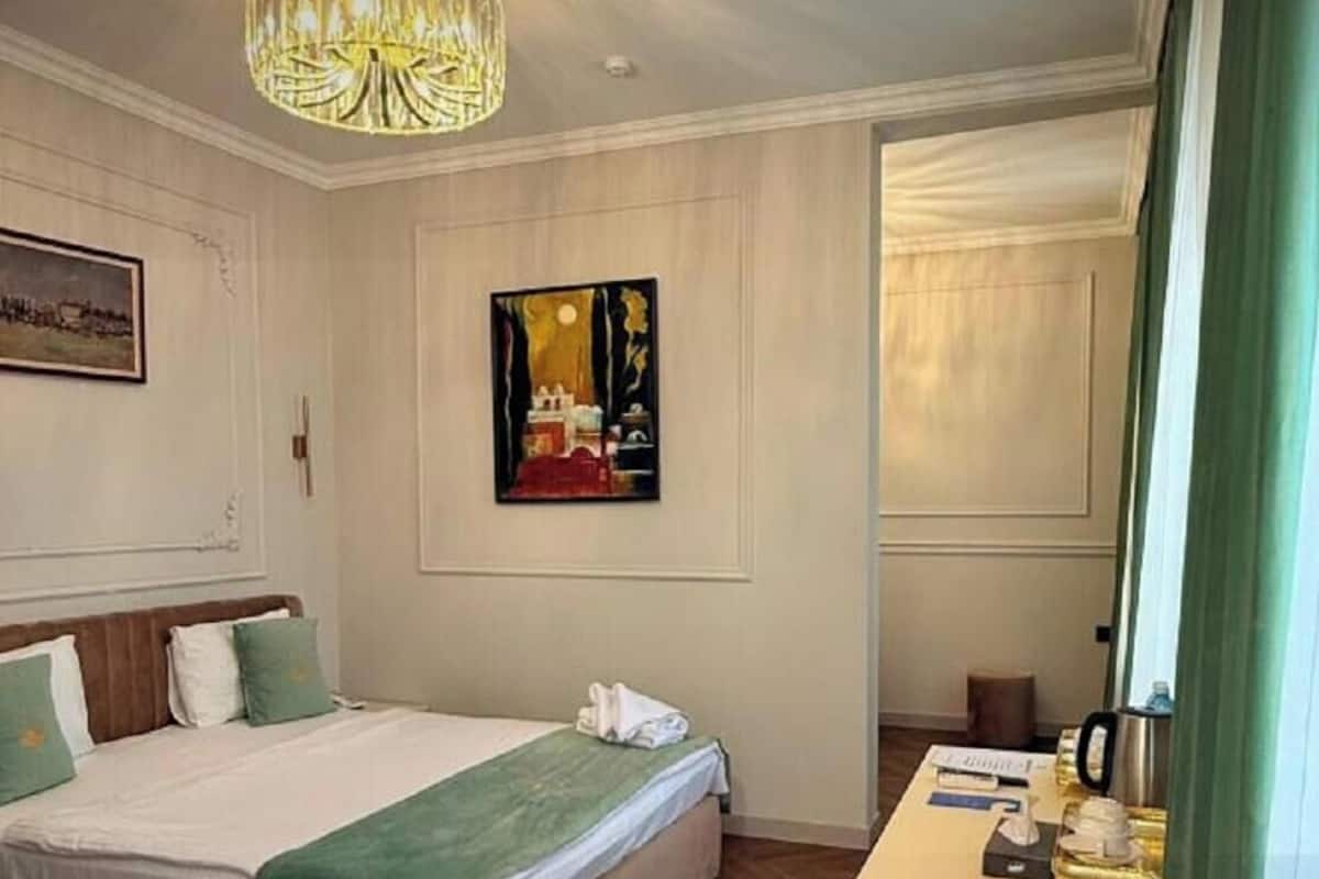 Une chambre d’hôtel avec un lit, un bureau doté d’une lampe, un tableau au mur et un lustre.