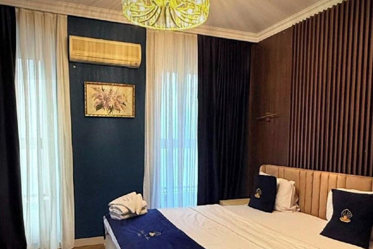 A hotel room with a large bed, a chandelier, a wooden headboard, and a framed picture on the wall.