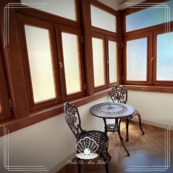 A room with a round table and two chairs, large windows with wooden frames, and a tiled floor.