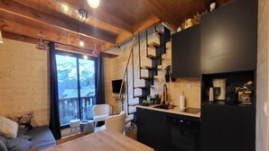Ein gemütliches Cabin-Interieur mit einem Holzesstisch, einer Couch, einer Küche mit schwarzem Kühlschrank und einer Treppe, die zu einem Balkon führt.