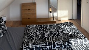 A bedroom with a sloped ceiling, a bed with a zebra-patterned bedspread, a wooden dresser, a mirror, and a ceiling-mounted light fixture. - Apartment 'Waldblick Alterkülz' with Wi-Fi (Alterkülz)
