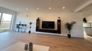 A spacious living room with a flat-screen TV, wooden flooring, and potted plants. - Apartment 'Waldblick Alterkülz' with Wi-Fi (Alterkülz)