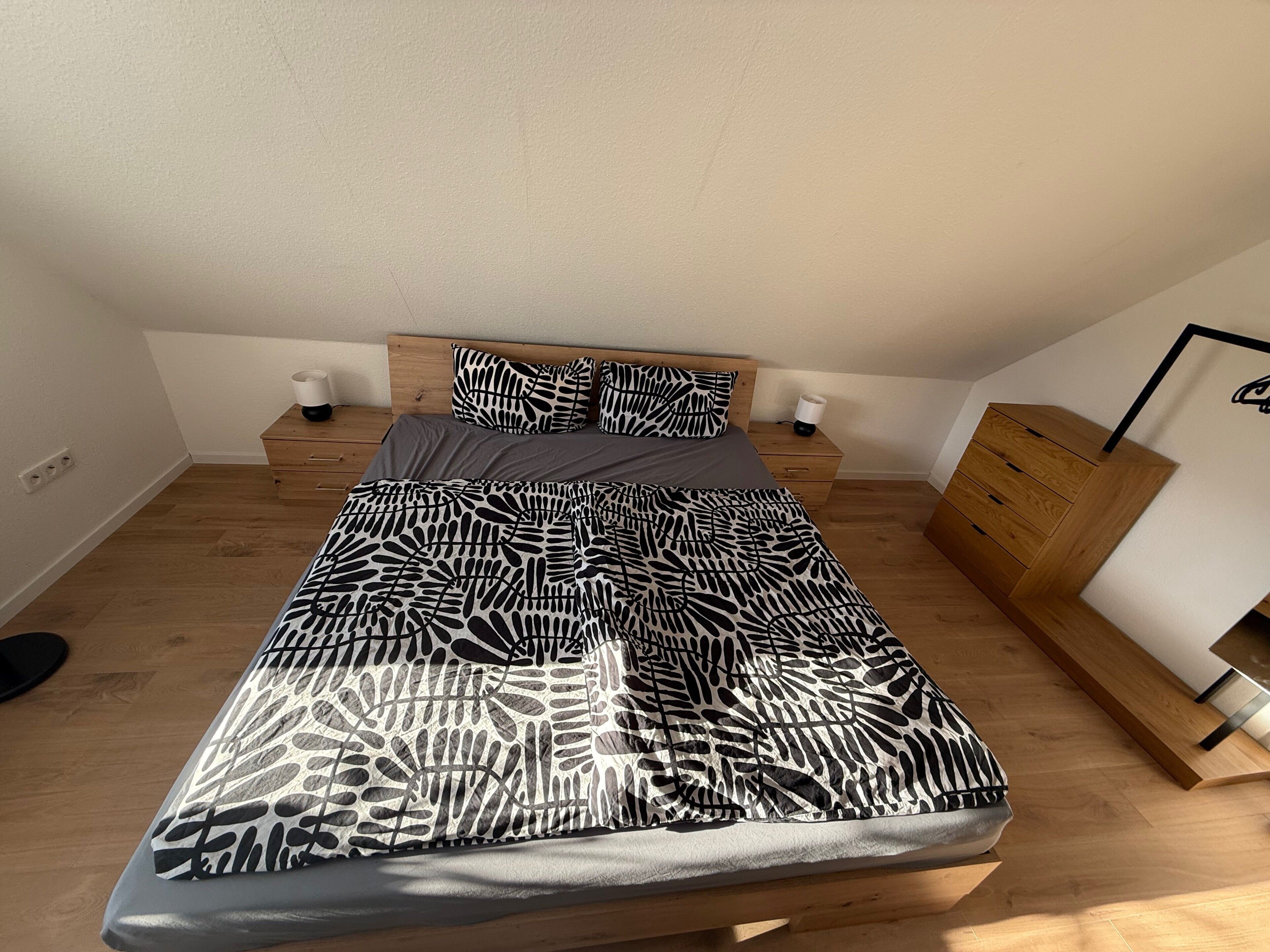 Ein Schlafzimmer mit einem Bett, Nachttischen, einer Kommode und einer Wandlampe.