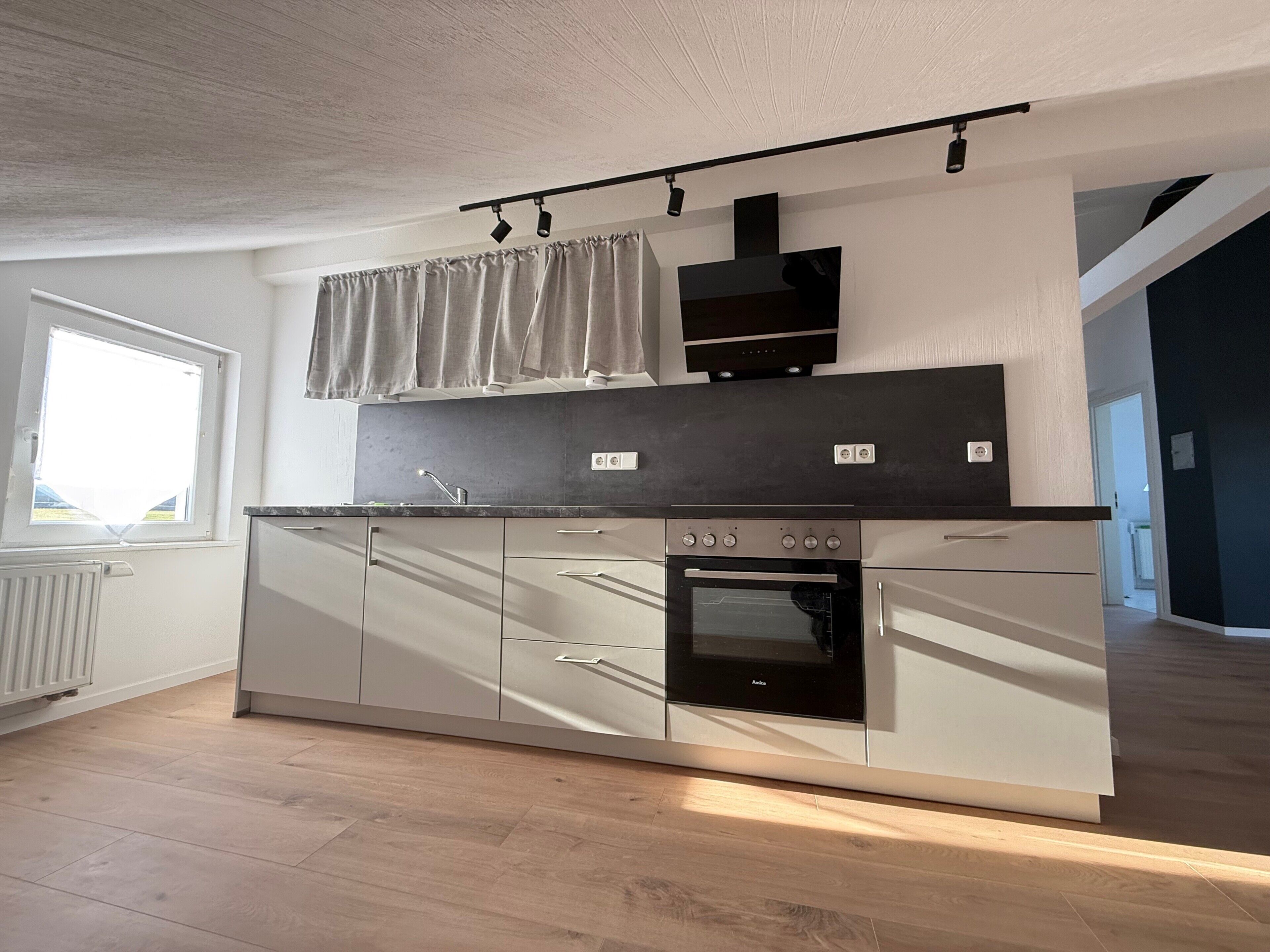 A modern kitchen with a built-in oven, a window with curtains, and a light-colored floor.
