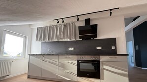 A modern kitchen with a built-in oven, a window with curtains, and a light-colored floor. - Apartment 'Waldblick Alterkülz' with Wi-Fi (Alterkülz)