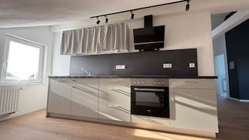 A modern kitchen with a built-in oven, a window with curtains, and a light-colored floor.