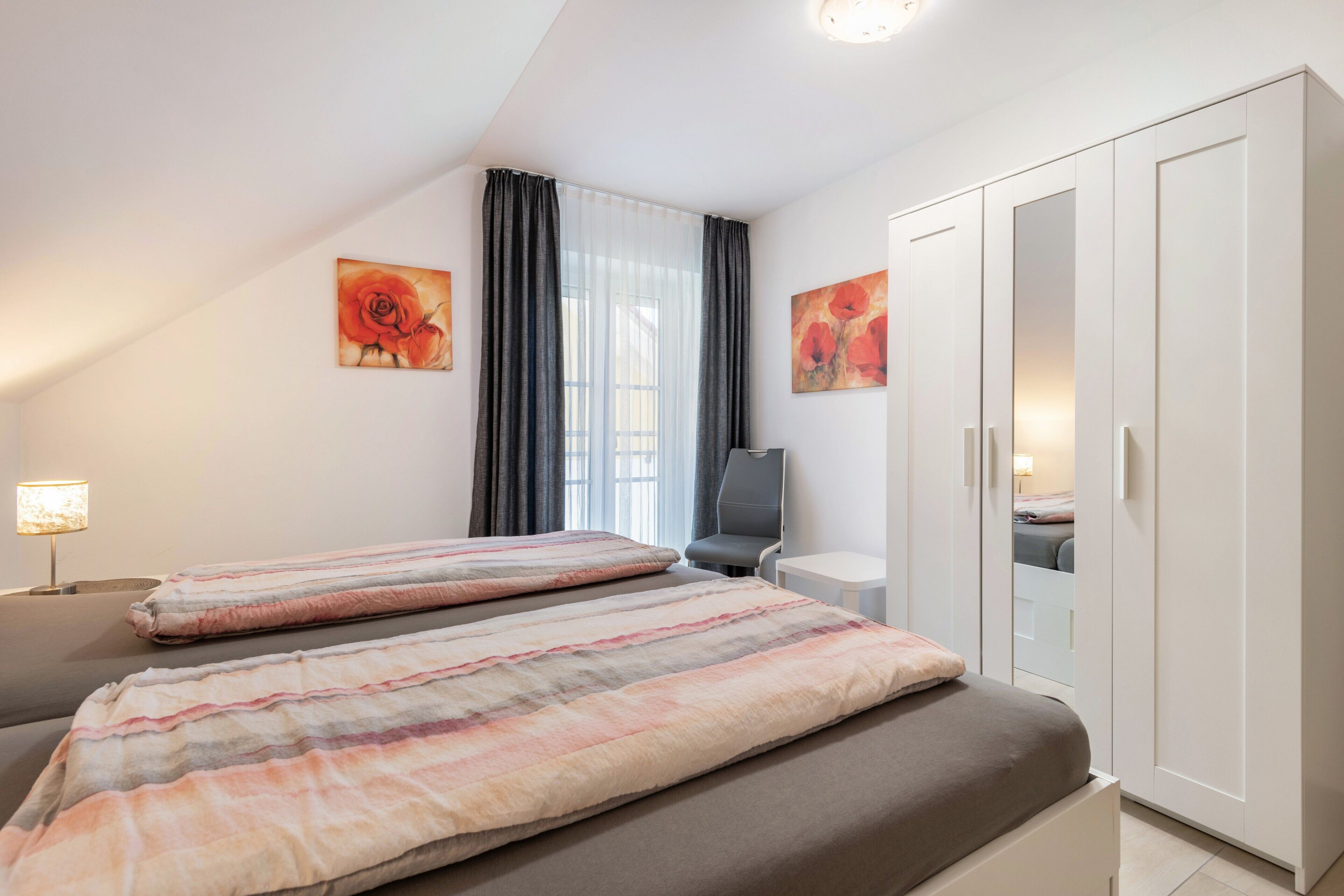 Ein Schlafzimmer mit zwei Betten, einem Schreibtisch, einem Stuhl, einem Kleiderschrank und Bildern an den Wänden.