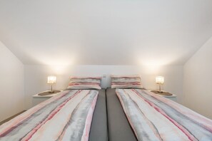 Une chambre double avec deux lits, chacun doté d’une table de chevet et d’une lampe, et un plafond blanc uni.