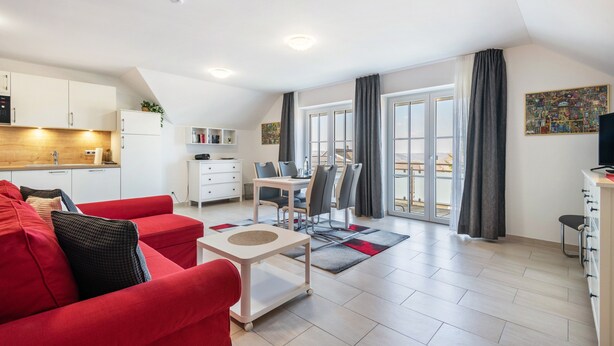 Um apartamento moderno com sofá vermelho, área de jantar, cozinha e varanda com cortinas.