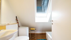 A small, bright bathroom with a toilet, sink, and bathtub. There's a window above the toilet and a small table with a towel. - Apartment 'C' with Wi-Fi (Bühl)