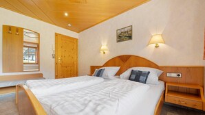 Une chambre à coucher avec un grand lit, une tête de lit en bois, des tables de chevet, une armoire en bois et une fenêtre avec des rideaux.