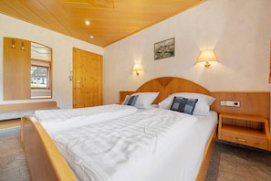 A bedroom with a large bed, wooden headboard, bedside tables, a wooden wardrobe, and a window with curtains.