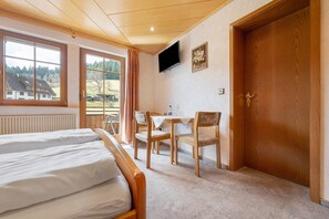 A hotel room with two beds, a desk, a chair, a television, and a door.
