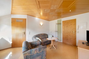 Una habitación con sofá, una mesita, televisor y puertas de madera.