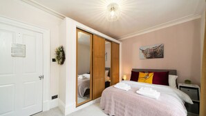 Ein Schlafzimmer mit Bett, Kleiderschrank, Spiegel, Gemälde und Nachttisch.