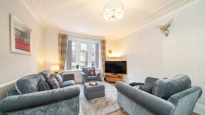 Ein Wohnzimmer mit zwei grauen Sofas, einem Couchtisch, einem Fernseher und einem aufgehängten Hirschkopf an der Wand.