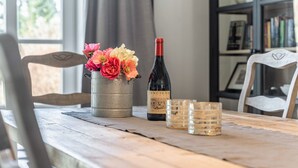 Une table en bois, une bouteille de vin, un seau en métal rempli de fleurs et deux verres transparents.