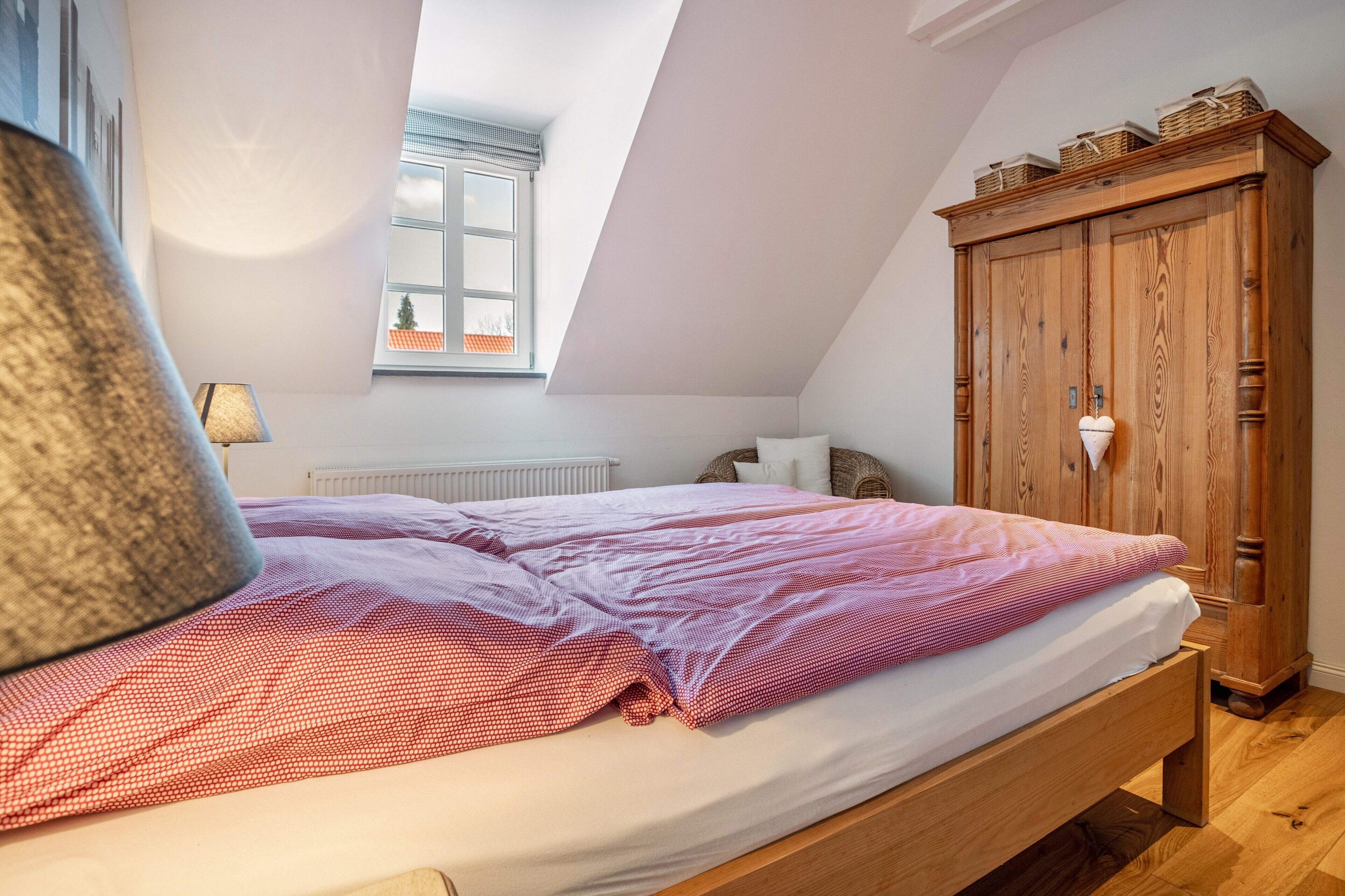 A bedroom with a wooden bed, a window with a view, a radiator, and a wooden wardrobe.