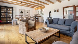 Un salon comprenant un canapé, un fauteuil en osier, une table basse en bois et un buffet contenant de la vaisselle.