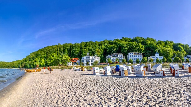 Une plage avec des cabanes de plage, un bateau en bois et des maisons sur une colline.