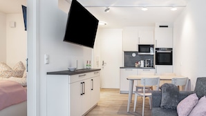 Una cocina moderna con armarios blancos, un televisor de pantalla plana y una zona de comedor con mesa y sillas.