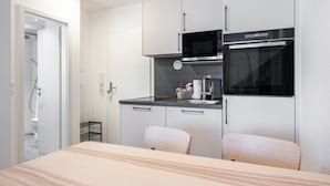 Cocina compacta con microondas, horno y lavabo. Zona de estar pequeña con mesa y sillas.