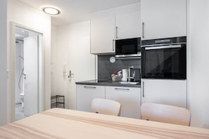 A compact kitchen with a microwave, oven, and sink. There is a small seating area with a table and chairs. - Holiday Apartment 'LeeKee' with Lake View, Balcony and Wi-Fi (Wunstorf)