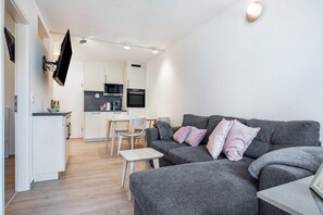 A modern living room with a grey sofa, a small table, and a flat-screen TV mounted on the wall. - Holiday Apartment 'LeeKee' with Lake View, Balcony and Wi-Fi (Wunstorf)