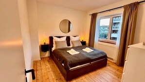 A bedroom with a bed, bedside lamps, a round mirror, a window with curtains, and a radiator. - Apartment 'The Pureness 1' with Shared Garden, Balcony and Wi-Fi (Hildesheim)